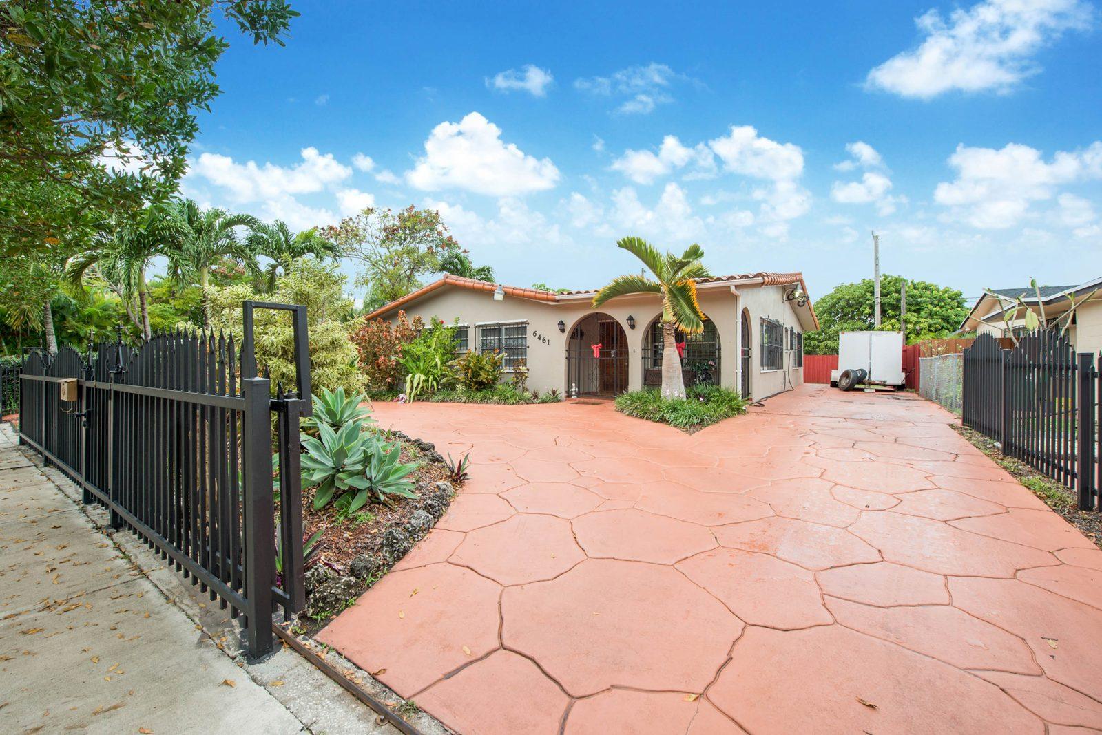 Single-story Spanish-style Miami home with arched entry and gated driveway, a typical long-held family home before downsizing
